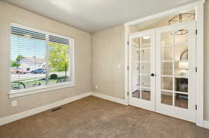 Carpeted empty room featuring french doors and baseboards