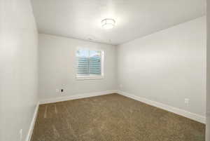 Empty room with dark carpet, baseboards, and a textured ceiling
