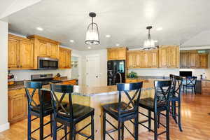 Kitchen with appliances with stainless steel finishes, light wood finished floors, recessed lighting, pendant lighting, and a breakfast bar