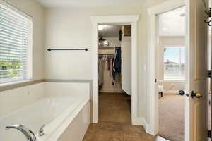 Full bath featuring a garden tub, tile patterned flooring, a walk in closet, and baseboards