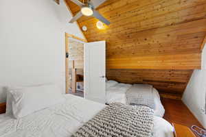 Bedroom with wood ceiling with exposed beams, wood walls, wood finished floors, a ceiling fan, and high vaulted ceiling