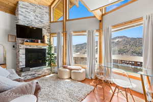 Living area with wood finished floors, a stone fireplace, high vaulted ceiling, and wood ceiling with exposed beams