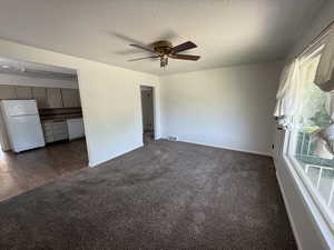 Unfurnished living room with dark carpet, a ceiling fan, baseboards, and a textured ceiling
