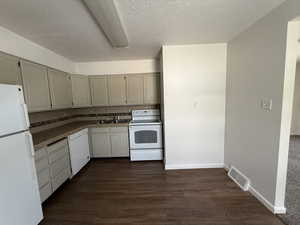 Kitchen featuring white appliances, tile counters, dark wood-type flooring, a textured ceiling, and a sink