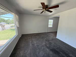 Empty room featuring dark colored carpet, a textured ceiling, ceiling fan, and baseboards