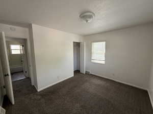 Unfurnished bedroom with multiple windows, dark carpet, baseboards, and a textured ceiling