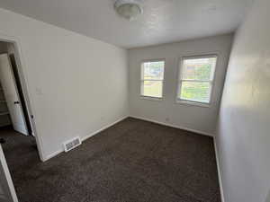Empty room with dark carpet, a textured ceiling, and baseboards