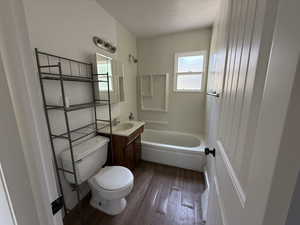 Bathroom with toilet, vanity, wood finished floors, shower / washtub combination, and a textured ceiling
