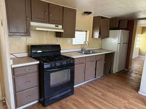 Kitchen with black range with gas stovetop, a sink, under cabinet range hood, light countertops, and a textured ceiling