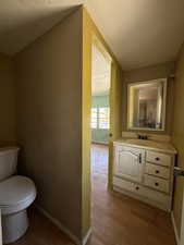 Half bath featuring toilet, vanity, baseboards, wood finished floors, and a textured ceiling