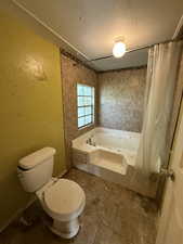 Bathroom with toilet, a combined bath / shower with jetted tub, a textured wall, tile patterned flooring, and a textured ceiling