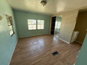 Unfurnished bedroom featuring a textured ceiling, multiple windows, wood finished floors, baseboards, and a closet
