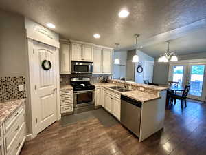 Kitchen with appliances with stainless steel finishes, a sink, a peninsula, a textured ceiling, and vaulted ceiling