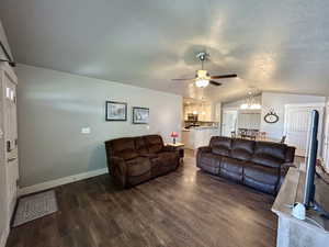 Living area with lofted ceiling, dark wood-type flooring, a chandelier, ceiling fan, and baseboards