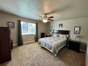 Bedroom with a textured ceiling, light carpet, baseboards, and a ceiling fan