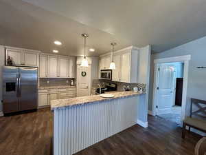 Kitchen with stainless steel appliances, dark wood-style flooring, a peninsula, tasteful backsplash, and recessed lighting