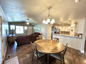 Dining room featuring dark wood-style flooring, ceiling fan, a textured ceiling, baseboards, and lofted ceiling