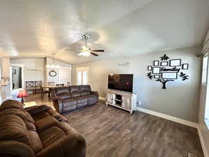 Living room featuring vaulted ceiling, dark wood-style floors, baseboards, a ceiling fan, and a textured ceiling