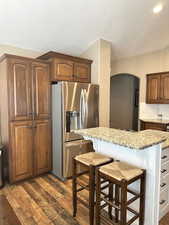 Kitchen featuring stainless steel fridge with ice dispenser, a kitchen bar, arched walkways, dark wood finished floors, and light stone counters