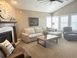 Living room featuring a ceiling fan, lofted ceiling, carpet, a brick fireplace, and a textured ceiling