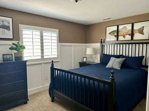 Bedroom with light colored carpet, a decorative wall, a wainscoted wall, and a textured ceiling