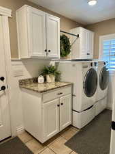 Washroom featuring washer and dryer, cabinet space, and light tile patterned floors