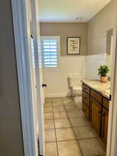 Bathroom featuring toilet, vanity, tile patterned floors, and a wainscoted wall