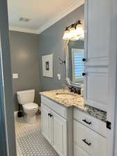 Half bathroom featuring vanity, toilet, crown molding, and tile patterned flooring