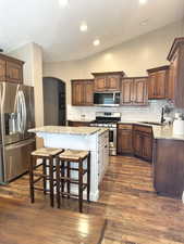 Kitchen featuring stainless steel appliances, arched walkways, a kitchen breakfast bar, tasteful backsplash, and light stone countertops