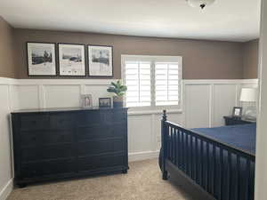 Bedroom featuring a decorative wall, light colored carpet, and a wainscoted wall