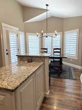 Kitchen with dark wood-style floors, vaulted ceiling, white cabinets, a chandelier, and light stone countertops