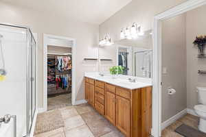 Full bath with a walk in closet, double vanity, toilet, a shower stall, and tile patterned flooring