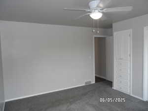 Main bedroom featuring dark colored carpet, baseboards, and ceiling fan