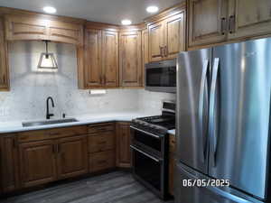 Kitchen featuring stainless steel appliances, backsplash, dark wood-style floors, and light countertops