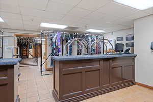 Gym with light tile patterned floors, a paneled ceiling, and baseboards
