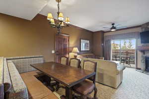Carpeted dining room with a chandelier, a ceiling fan, crown molding, and a stone fireplace
