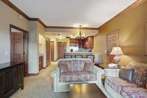 Living room with ornamental molding, a chandelier, baseboards, and light colored carpet