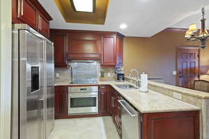 Kitchen with stainless steel appliances, a sink, a peninsula, reddish brown cabinets, and custom exhaust hood