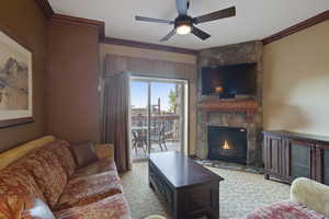 Living area with crown molding, a ceiling fan, and a stone fireplace