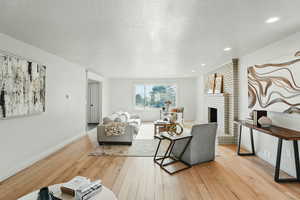 Living room featuring light wood-style flooring, a brick fireplace, a textured ceiling, and baseboards