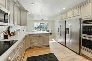 Kitchen with stainless steel appliances, a peninsula, cream cabinets, recessed lighting, and light wood finished floors