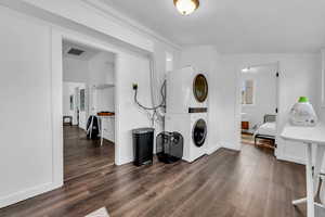 Washroom featuring stacked washer / drying machine, dark wood-style floors, and baseboards