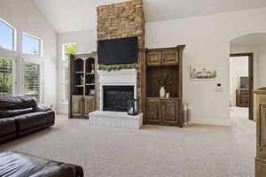 Living room with a large fireplace, light carpet, arched walkways, baseboards, and high vaulted ceiling