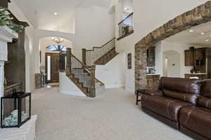 Living area with arched walkways, light colored carpet, stairway, a chandelier, and a high ceiling