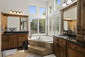 Full bath featuring stone tile floors, two vanities, a bath, and a high ceiling