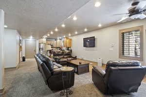 Living area featuring a textured ceiling, recessed lighting, light carpet, ceiling fan, and baseboards