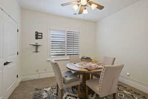 Carpeted dining area with ceiling fan and baseboards