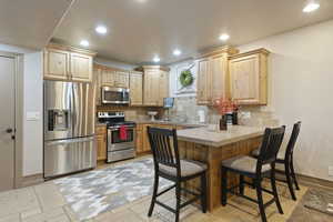 Kitchen with appliances with stainless steel finishes, light brown cabinetry, a peninsula, a kitchen bar, and decorative backsplash