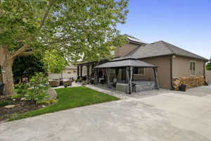 Back of house featuring outdoor lounge area, a gazebo, a patio, stucco siding, and a hot tub