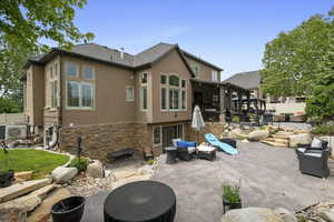 Back of house featuring stucco siding, a patio area, stone siding, a cooling unit, and an outdoor living space with a fire pit